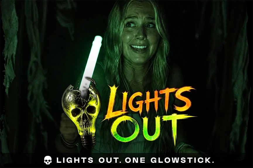 A terrified young woman clutches a single, glowing green lightbulb in pitch darkness. The text reads "Lights Out. One Glowstick."